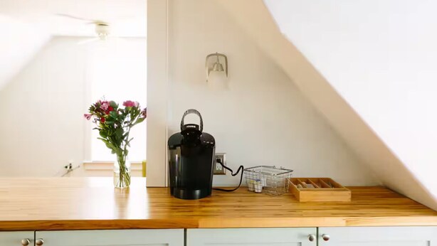 Une cuisine avec un plan de travail en bois, une bouilloire noire, un vase rempli de fleurs et un petit panier en fil de fer.