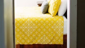 Une chambre à coucher avec une couvre-lit jaune à motifs, un oreiller blanc et un oreiller gris.