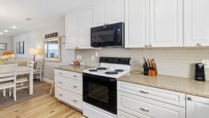 Una cocina moderna con armarios blancos, un microondas negro, una estufa y una encimera con un juego de cuchillos.