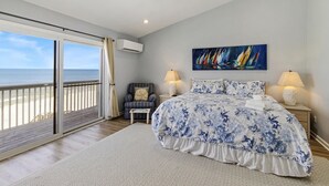 Un dormitorio con una cama grande, una silla, un cuadro y vista al océano.