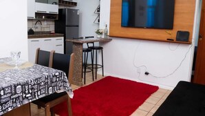 Une cuisine compacte dotée d’un réfrigérateur intégré, d’un coin repas agrémenté d’un tapis rouge et d’un téléviseur fixé au mur.