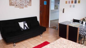 Un salon avec un canapé noir, une table à manger avec des chaises et un tapis rouge. On y trouve également des éléments de décoration murale et une porte avec une pancarte.