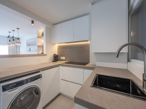 A modern kitchen with a built-in washing machine, a coffee machine, and a sleek stainless steel sink. - Modern Seaside Escape (Knokke-Heist)