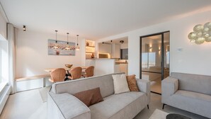 Un salon moderne avec un canapé, un coin repas avec des chaises et une cuisine en arrière-plan.