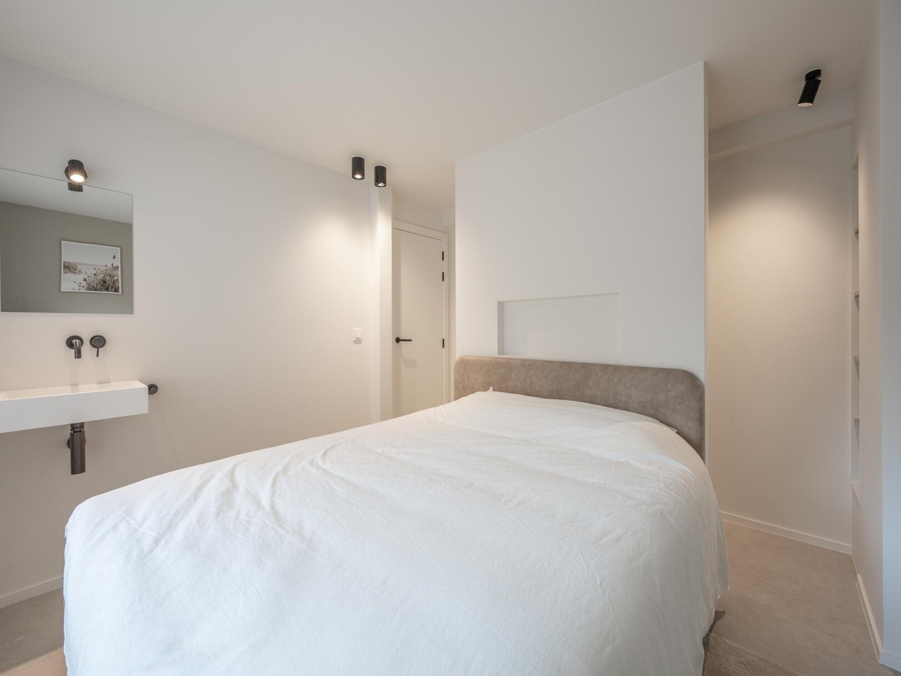 Een moderne slaapkamer met een bed, nachtkastje, spiegel en een deur.