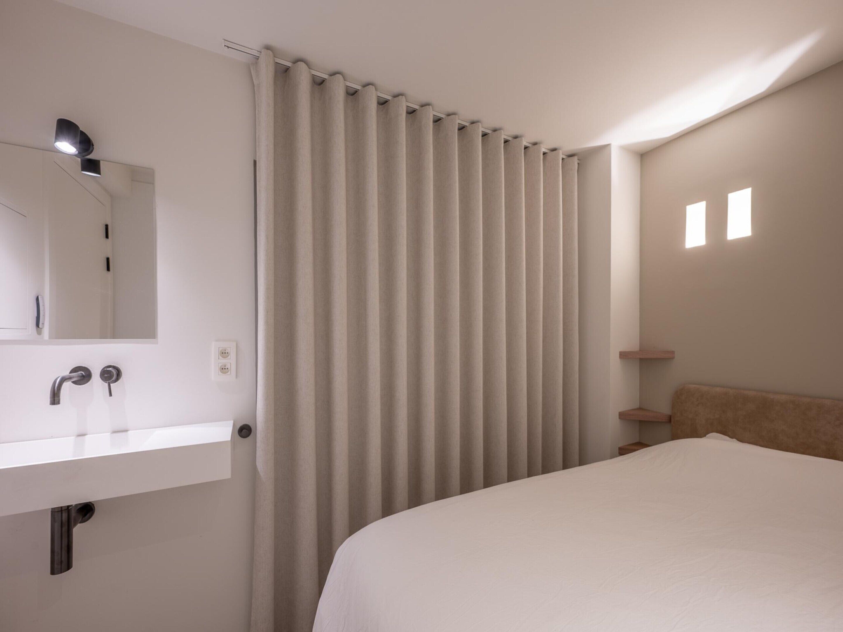 A hotel room with a bed, a bathroom with a sink and mirror, and a window with curtains.