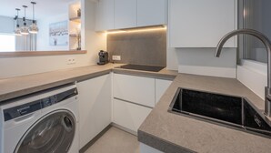Une cuisine moderne équipée d’un lave-linge encastré, d’une machine à café et d’un élégant évier en acier inoxydable.