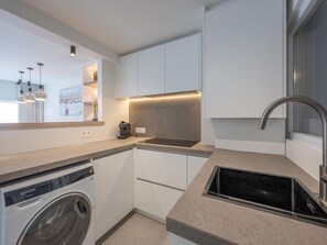A modern kitchen with a built-in washing machine, a coffee machine, and a sleek stainless steel sink. - Modern Seaside Escape (Knokke-Heist)
