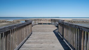 Een houten looppad dat naar een strand leidt, onder een heldere lucht.