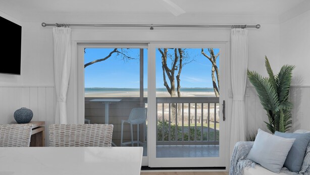 Een kamer met een grote schuifglazen deur die uitkomt op een balkon met uitzicht op het strand.