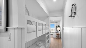 Een moderne hotelkamer met stapelbedden, een flatscreen televisie, een klein tafeltje met lamp en uitzicht op zee.