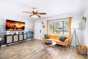 A living room with a sofa, a coffee table, a television, and a ceiling fan.