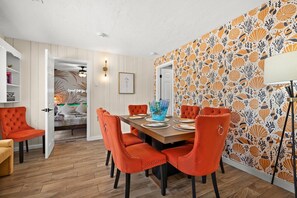 A dining area with a wooden table, orange upholstered chairs, and a patterned wallpaper.