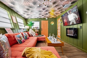 A room with a sectional sofa, a wooden coffee table, a television mounted on the wall, and a patterned ceiling.
