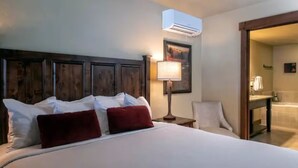 A hotel room with a large bed, a wooden headboard, a bedside table with a lamp, and a bathroom visible through an open door. - 4th of July in Breckenridge at Grand Lodge on Peak 7 (Breckenridge)