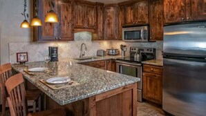 A kitchen with wooden cabinets, granite countertops, stainless steel appliances, and pendant lighting. - 4th of July in Breckenridge at Grand Lodge on Peak 7 (Breckenridge)