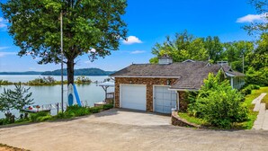 A lakeside house with a stone exterior, two garage doors, and a dock with kayaks. - Lakefront Oasis- Steps to Water- Private Boat Ramp (Dandridge)