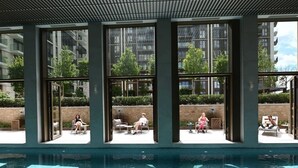 A pool area with clear glass walls, allowing views of the surrounding buildings and greenery.