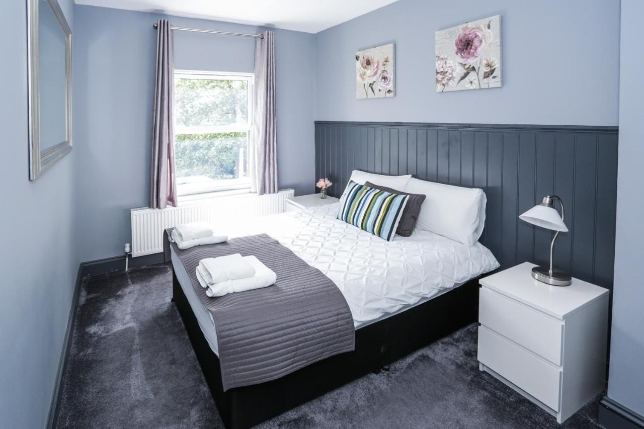 A bedroom with a bed, bedside tables, a radiator, a window with curtains, and wall art.
