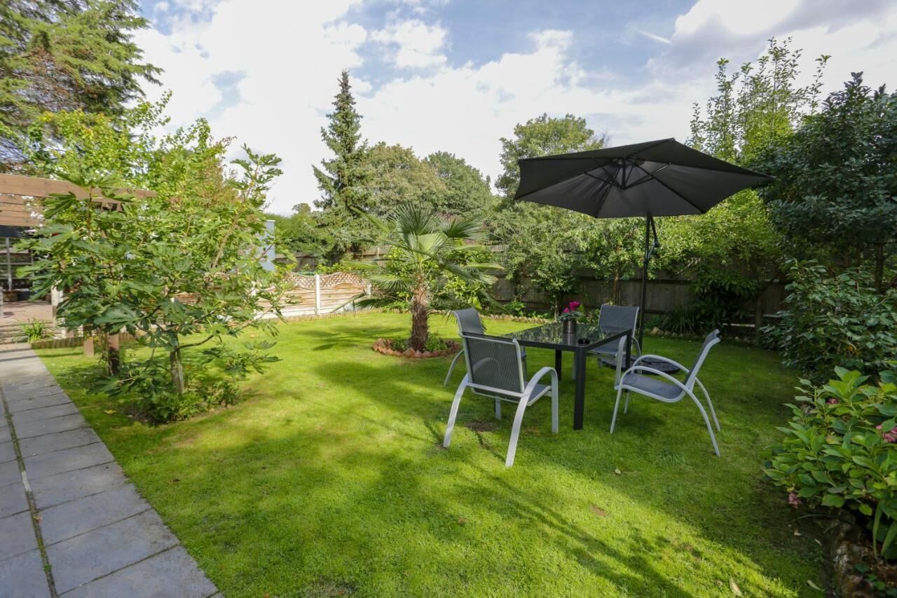 A patio with a table and chairs, surrounded by lush greenery and a wooden fence.