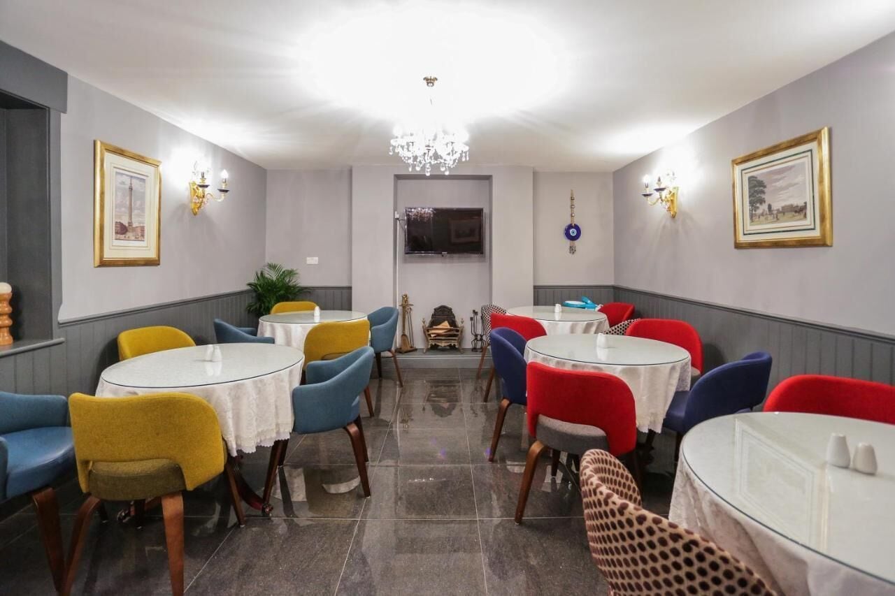 Un comedor con mesas y sillas redondas, una araña y cuadros en las paredes.