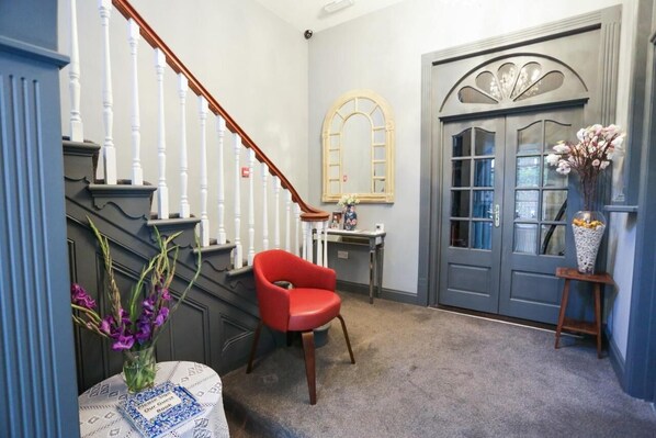 A hallway with a staircase, a red chair, a vase with flowers, and a door with glass panels. - Beckenham Park Hotel (Beckenham)
