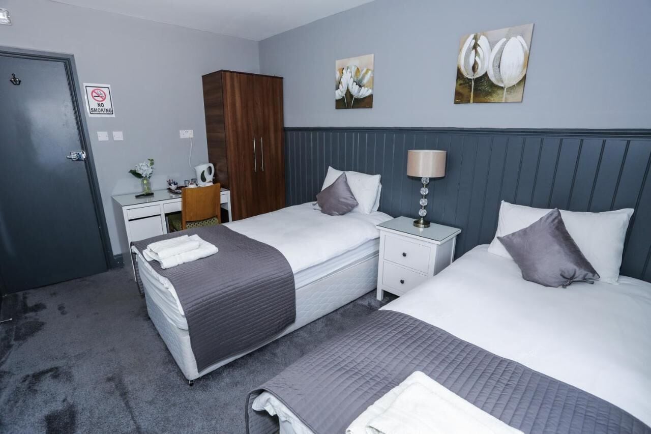 A hotel room with two beds, a desk, a wardrobe, and a "No Smoking" sign.