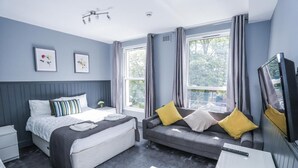 A bedroom with a bed, a sofa, a TV, and a window with curtains. - Beckenham Park Hotel (Beckenham)