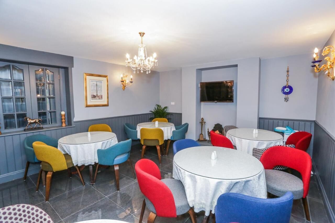 A dining area with round tables and colorful chairs, a chandelier, and a TV mounted on the wall.