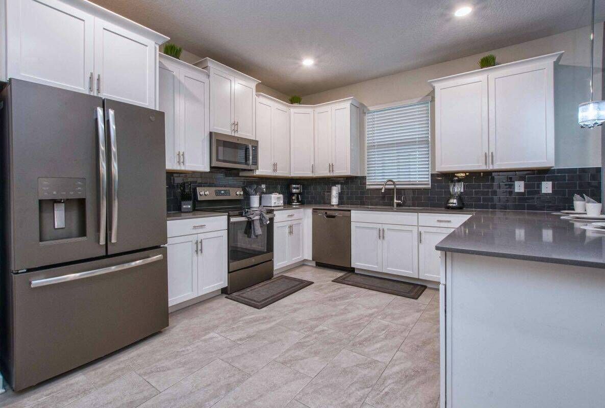 Une cuisine moderne avec des armoires blanches, des appareils en acier inoxydable et un dosseret de carrelage noir.