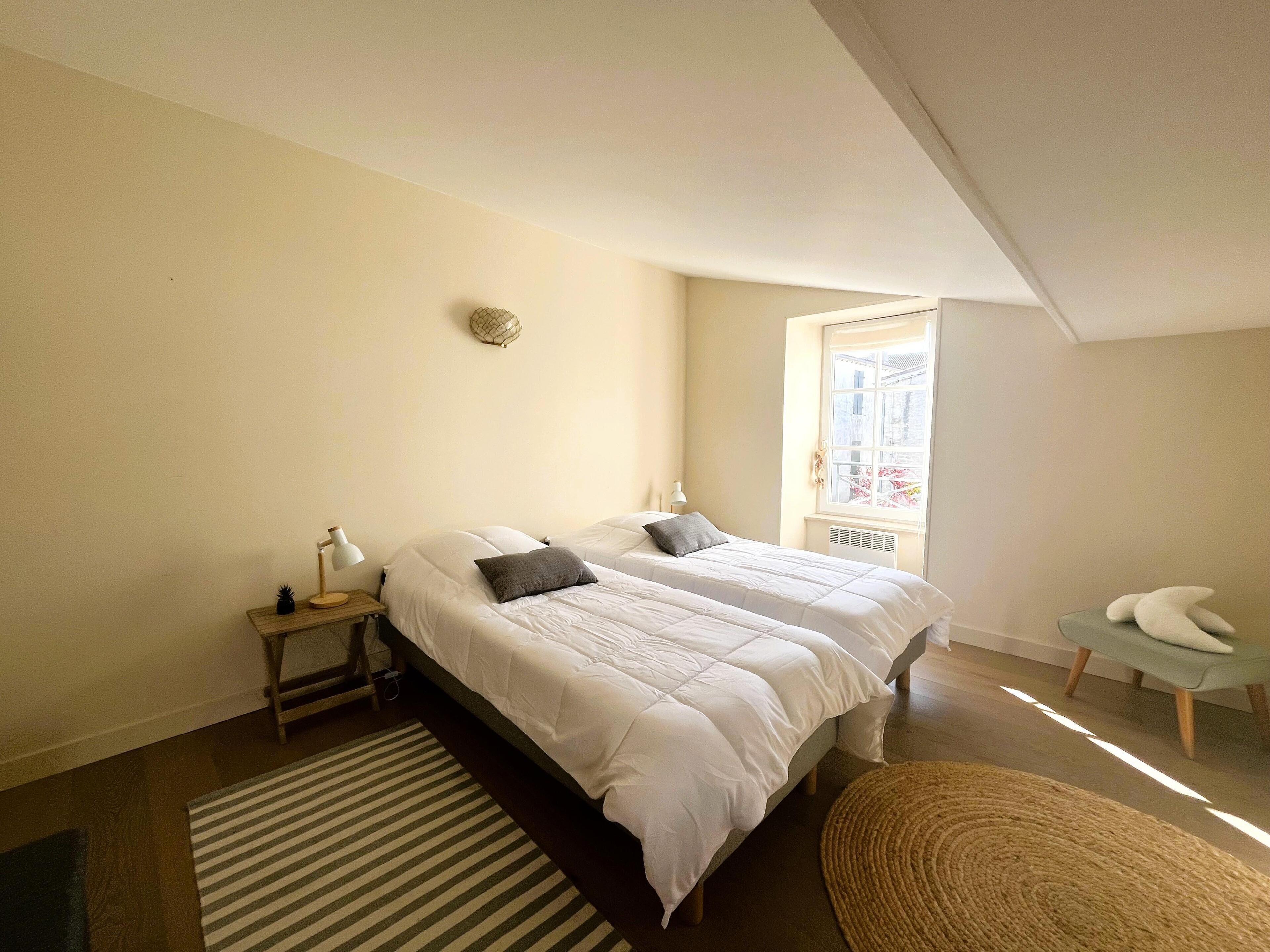 Une chambre avec deux lits, une table de chevet avec une lampe, une fenêtre donnant sur un beau paysage et un fauteuil.