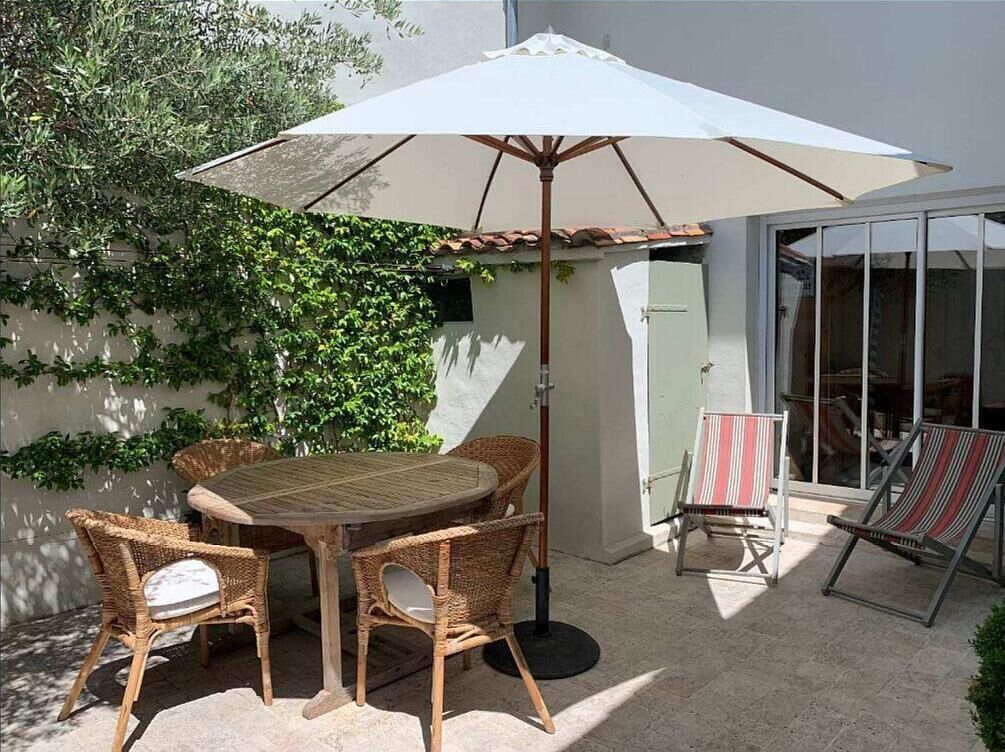 Un patio con un tavolo rotondo e sedie in vimini, un ombrellone e una porta vetrata che dà su una stanza.