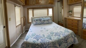 A bedroom with a bed, a dresser, and a window with blinds.