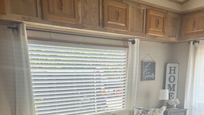 A beige sectional sofa with blue and white patterned pillows, a wooden cabinet, and a window with blinds.