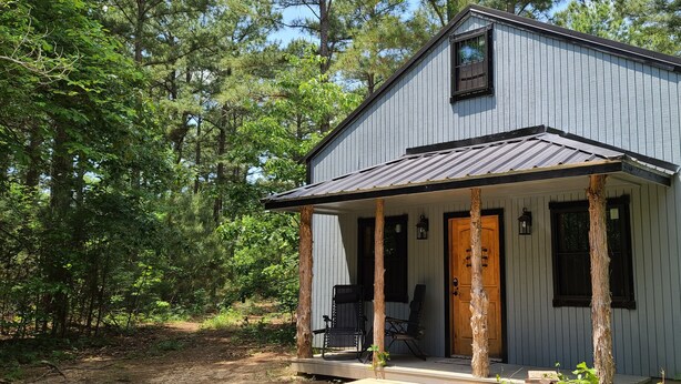 A small, single-story cabin with a porch, surrounded by trees. - Hidden in East Texas Piney Woods - Rustic Western Cabin - Canton 1st Monday (Mineola)