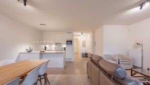 A modern kitchen with white cabinets, a wooden dining table, and a built-in bench with leather seating. - Apartment in Knokke Near the Beach & Casino (Knokke-Heist)