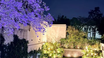 Un jardín ajardinado con césped cuidado, diversas plantas y un gran árbol con flores moradas.