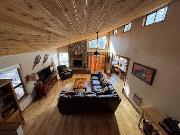 A spacious living room with a stone fireplace, wooden ceiling, and large windows. - Relaxing mountain escape, fully stocked, with Wi-Fi in Pinetop Country Club (Pinetop Country Club)