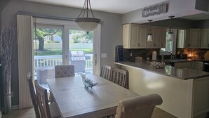 Une cuisine moderne dotée d’un îlot central, d’un coin repas avec une table et des chaises blanches, et offrant une vue sur l’extérieur grâce à une porte-fenêtre coulissante.