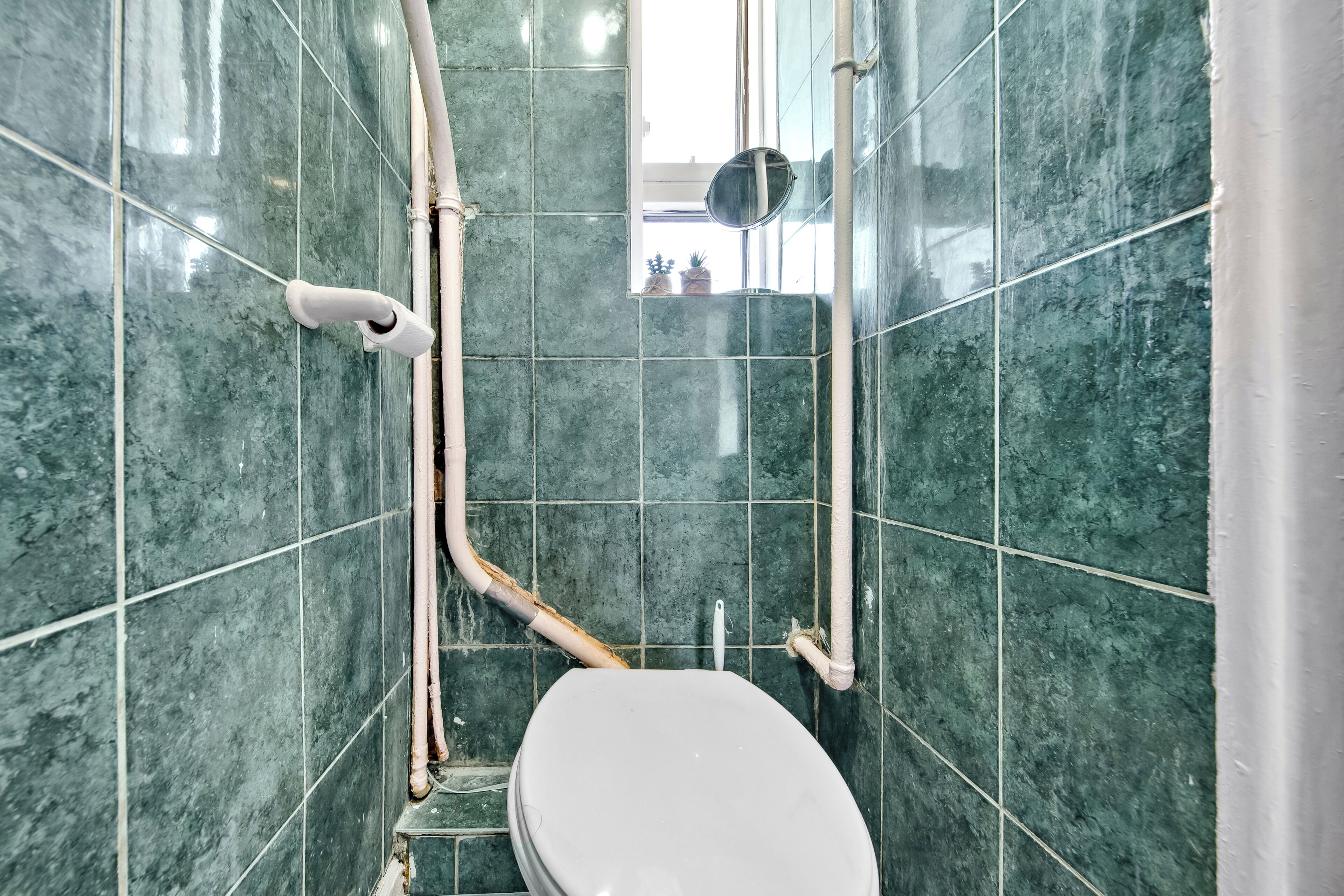 Une salle de bain avec des carreaux de marbre vert, des toilettes blanches et des tuyaux apparents.