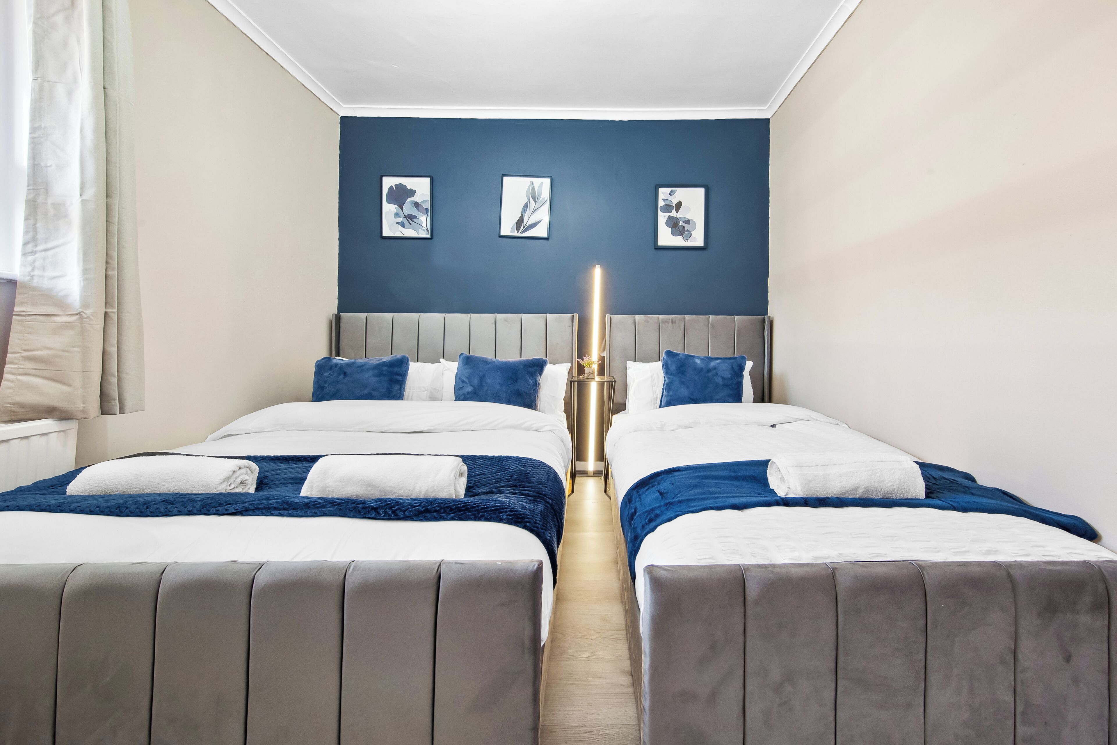 Habitación de hotel con dos camas, cabecero gris y pared azul de acento.