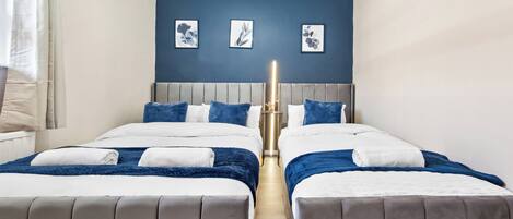 Habitación de hotel con dos camas, cabecero gris y pared azul de acento.