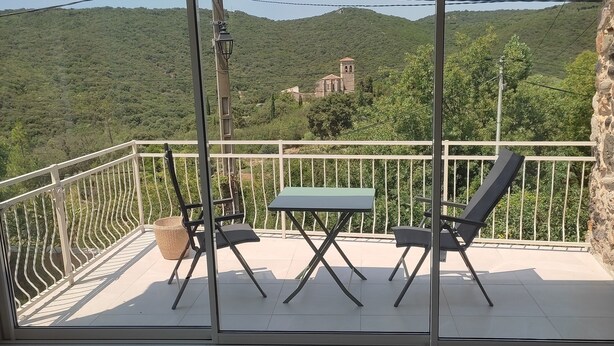 A balcony with a table and chairs, a view of a green landscape with a building in the distance. - House in a charming village in the countryside, near the Olivettes Dam (Vailhan)
