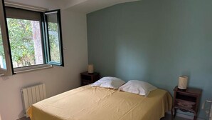 A bedroom with a bed, a window, a radiator, and a nightstand with a lamp. - House in a charming village in the countryside, near the Olivettes Dam (Vailhan)
