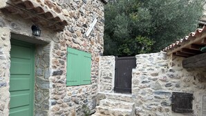 A stone building with a green door and a small set of steps leading to a dark door. - House in a charming village in the countryside, near the Olivettes Dam (Vailhan)