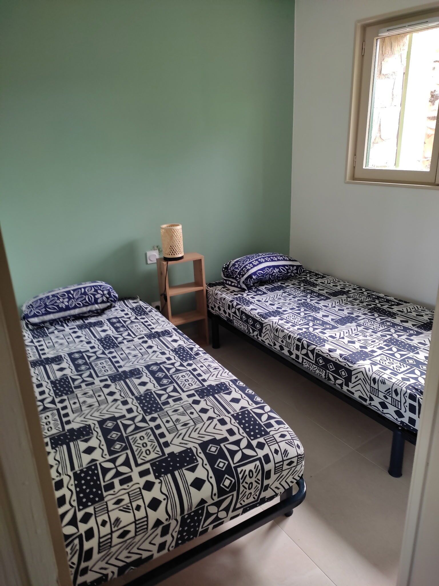 Una habitación con dos camas individuales, un pequeño estante de madera y una ventana.