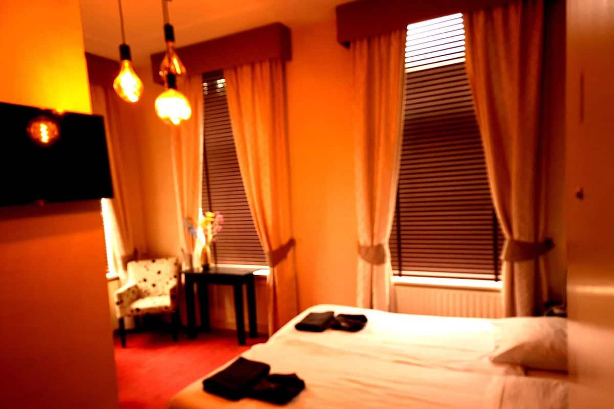 Quarto de hotel com cama, uma cadeira, uma mesa pequena e uma escrivaninha.