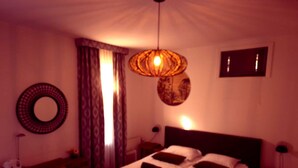 Un dormitorio con una cama, un espejo redondo, una mesita de noche y una lámpara colgante.