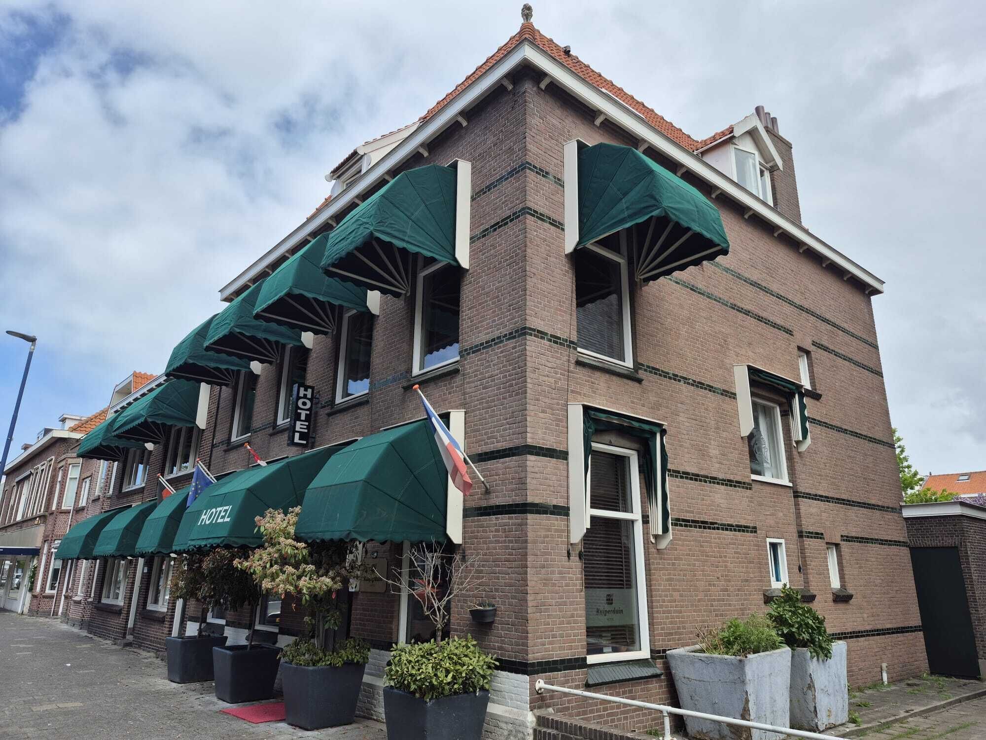 Ein Hotel mit Backsteinfassade, grünen Markisen und zahlreichen Fenstern.
