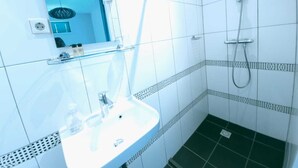 Un baño con lavamanos blanco, espejo, ducha y piso de baldosas.